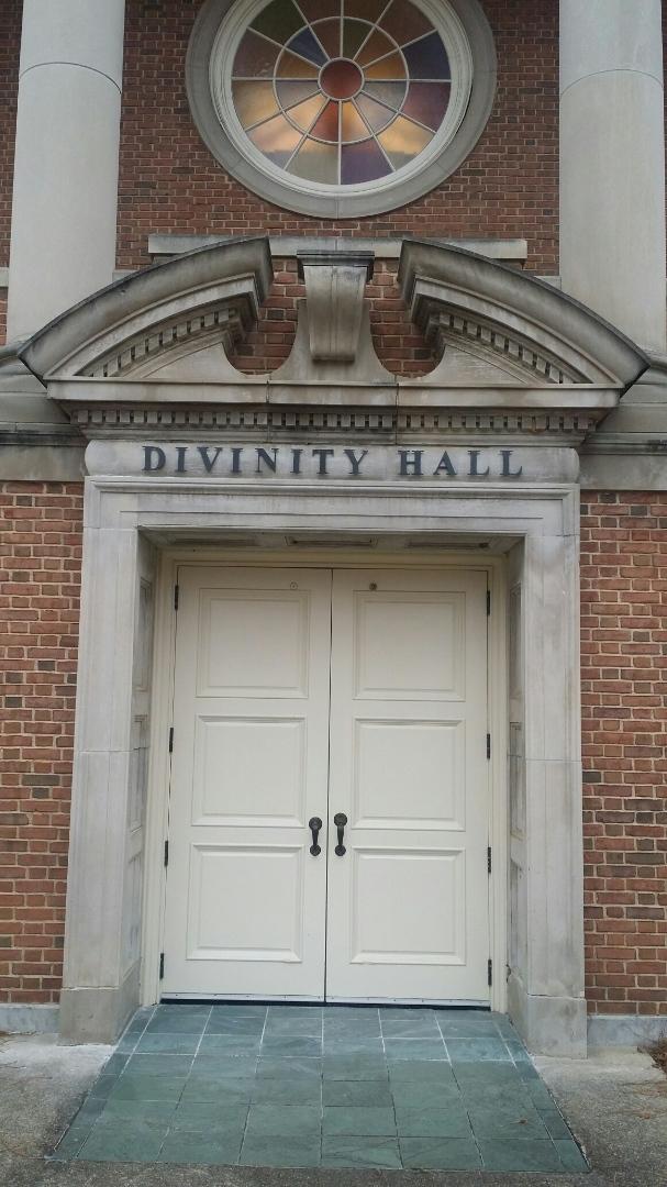 A photo of a doorway on a red brick building with the words "Divinity Hall" mounted above the doorframe